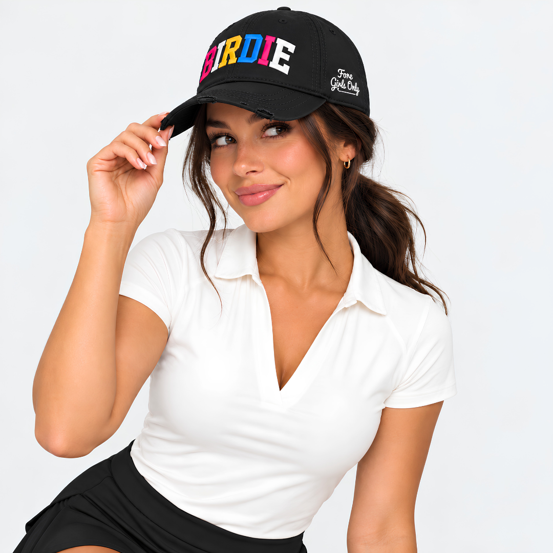 A woman wearing a black baseball cap with colorful 'BIRDIE' lettering and a white polo shirt, posing against a light gray background.