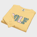 A folded pale yellow sweatshirt on a white background, featuring a large collegiate-style 'GOLF' graphic across the chest with alternating green-and-white checkered and pink-and-white striped letters.