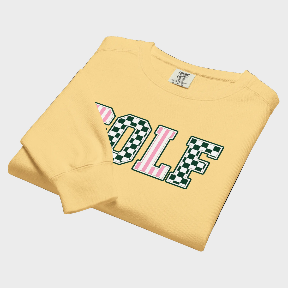 A folded pale yellow sweatshirt on a white background, featuring a large collegiate-style 'GOLF' graphic across the chest with alternating green-and-white checkered and pink-and-white striped letters.