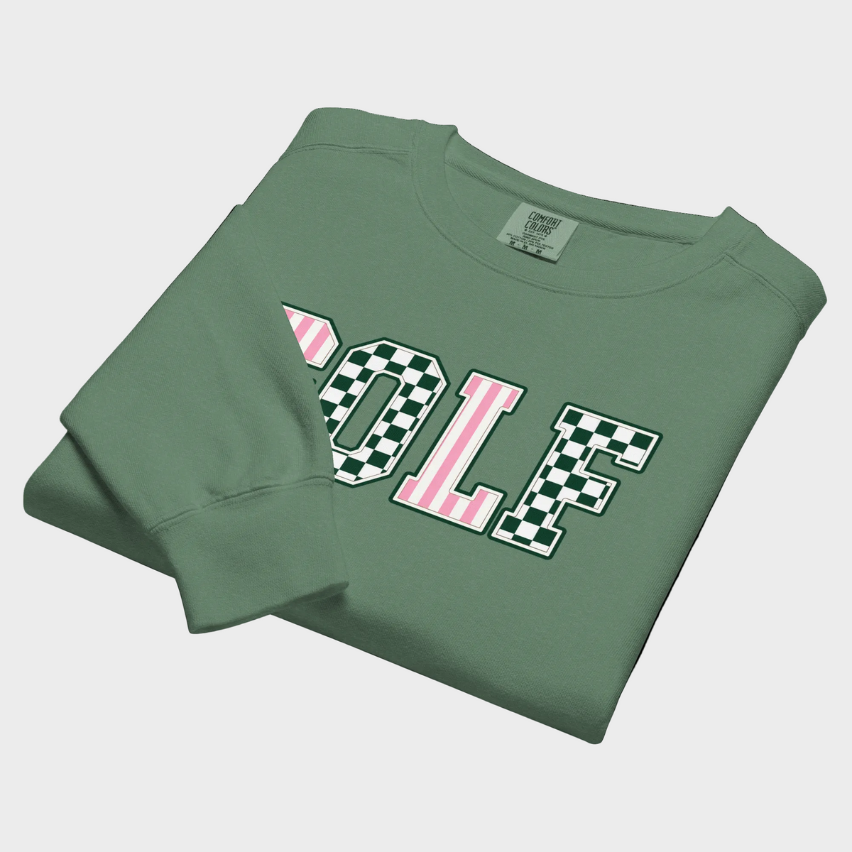 A folded sage green crewneck sweatshirt featuring the word 'GOLF' printed across the chest in varsity block letters. The letters are filled with pink vertical stripes and black-and-white checkerboard patterns, outlined in white.
